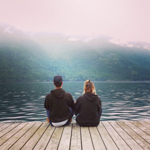 Two people sitting on a dock overlooking Kootenay Lake